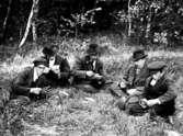 Fem män sitter i gräset och spelar kort.