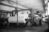 Man i arbete vid rullmaskin 5, byggnad 10 på pappersbruket Papyrus i Mölndal, hösten 1970. Mannen på bilden arbetar som rullare och sköter maskinen med hjälp av manöverbord.