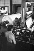 Män i arbete vid rullmaskin 5. Pappret rullas upp och skärs till rätt rullbredd. På bilden syns maskinens styrpulpet/manöverpulpet. Byggnad 10. Pappersbruket Papyrus i Mölndal, hösten 1970.