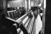 Män i arbete vid maskin på pappersbruket Papyrus i Mölndal, hösten 1970. RM 5, byggnad 10. I bakgrunden syns PM 12 (senare PM 7).