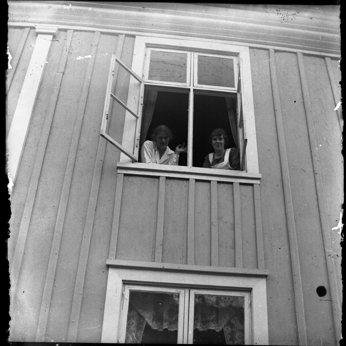 Unknown artist, Två okända kvinnor tittar ut genom ett fönster på andra våningen. Kvinnan till vänster vinkar mot fotografen. Kvinna till höger ser ut att han förkläde på sig, någon form av arbetsklädsel.