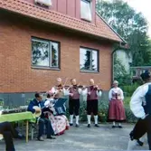 Midsommar och underhållning av Hällesåkers Folkdanslag utanför ålderdomshemmet Brattåshemmet 1980. Spelmännen (både kvinnor och män) är folkdräktsklädda.