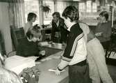 Biblioteksassistent Ingrid Hansson (sittande till vänster) vid utlåningsdisken på Kållereds bibliotek 1980-tal.