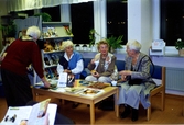 Fyra kvinnor samtalar bland hyllorna, Kållereds bibliotek 1990-tal. Ett arrangemang anordnat av Hembygdsföreningen. Sittande i soffan, från vänster: Nancy Ehrenborg, Majken Olsson samt okänd.