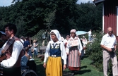 Dräktparad med folkdräktsklädda män och kvinnor en hembygdsdag på Långåker år 1984. I mitten ses Karin Gustafsson hållandes en Skåne-skylt.