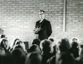 Biskop Bo Giertz står med en uppslagen bok i händerna framför skoleleverna i Församlingshemmet vid Biskopsvisitationen år 1966.