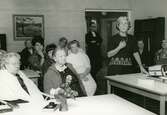 Diabildsvisning av prästfrun Märta Lindman i matsalen på Brattåshemmets ålderdomshem, 1960-tal. Från vänster: 1. Mathilda Bengtsson (född Apel 1894 - 1968 Dammkärr), 2. Okänd, 3. vårdbiträde Lena Englund Söderberg, 4. Okänd, 5. Selma Börjesson (Hökkullen), 6. Okänd, 7 vårdbiträde Asta Ögren, 8. komminister Gustaf Lindman (står i dörren), 9. hustrun Märta Lindman, 10. Ulla Eklund (Sagered) från socialnämnden samt 11. Olga Holmén (Vommedal).