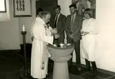 Kyrkoherde Gustaf Lindman döper ett litet barn i Kållereds kyrka efter år 1976. Okända personer i bakgrunden.