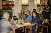 Fikastund i Brattåsgårdens café där girlanger hänger i taket, 1990-tal. I mitten från vänster: Berta Mattsson (vid fönstret), Sigrid Olsson (med mörkblå rosett) och Maria Brattberg (i mörkblå klänning). Den röda tegelbyggnaden som skymtas utanför är Vommedalsområdet och Kållereds centrum.