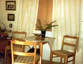 Brattåsgården vid invigningen år 1986. Utställning av föremål från gamla Brattåshemmet, gjord av Kållereds Hembygdsgille. Delar av föremålen finns nu på Mölndals stadsmuseum. Här ses ett litet fyrkantigt bord och tre stolar, allt i ljust trä.