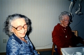 Marianne Skarin och Helfrid Kristensson sitter och fikar i Brattåsgårdens matsal på Streteredsvägen 5, cirka 1990. En girlang hänger från taket.