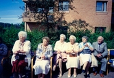 Sex äldre personer sitter utomhus då det firas midsommar utanför Brattåsgården, cirka 1986 - 1990. Från vänster: Aina Olsson (1917 - 2007), Sonja Yngvall (1921 - 2004), Karin Zackrisson, Märta Andersson samt okänd kvinna och man till höger.