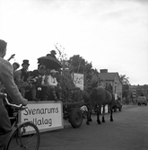 Utklädda passagerare i en hästdragen lövad vagn i Jönköping att dömma av gaslyktan. Kanske Tullportsgatan norrut. En skylt sitter på vagnen med texten 