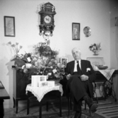 Bredvid bordet med blommor och gratulationskort sitter Komminister Ragnar Nordh i Jönköping på sin högtidsdag. Han arbetade  som komminister i Ödestugu mellan åren 1954 - 1959. Han var sedan verksam i Kristina och Ljungarums församlingar och i Österängskyrkan på 1960-talet.