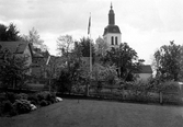 Gränna kyrka bakom några hus med trädgårdar.