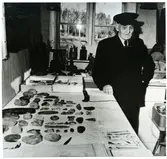 Tortuna sn, Västerås kn, Ängesta.
J. L. Andersson vid bord med fornfynd, 1958.