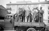 En lastbil från Gunnebo Bruk. I förarhytten sitter chauffören och på flaket står sex kostymklädda män.