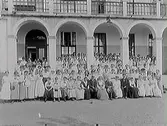 Sommaravslutning. Elever och lärare framför en arkad på Katrinebergs folkhögskola (troligen).  Många personer i bild, de flesta kädda i ljusa sommarkläder.