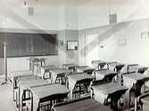 Skolsal med skolbänkar och skrivtavla (den sk svarta tavlan) på väggen.  Falkenbergs kommunala mellanskola. Interiör.