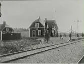 Invigningen av järnvägslinjen Varberg-Ätran. Järnvägsstationen i Grimeton, fotograferat från spårområdet. Intill stationsbyggnaden står ett bostadshus. Några personer väntar på perrongen.