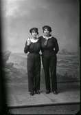 Två unga kvinnor i marina dräkter som då var på modet; här klädda i byxor och mössor. Ateljébild.