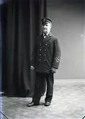Mansporträtt, man stående i helfigur iklädd lotsuniform med skärmmössa. Ateljébild.