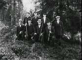 Ett jaktlag poserande i skogen med gevär. Med på bilden är bland andra Robert Johansson och Gusten Gustafsson. Männen bär huvudbonader av olika modeller.