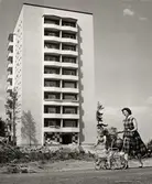 Kvinna med barnvagn promenerar framför nybyggt höghus i Stockholmsförorten Fruängen.