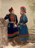 Studiofotografi av sameflickorna Inga Åren, Frostviken, Jämtland och Maria Ringdal, Hultfjället, Lappland. Handkolorerat ateljéporträtt i helfigur.