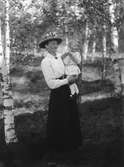 Anna Bergström i lång kjol, blus med brosch i halsen och hatt. På armen bär hon barnet Stig Trogen f. 1917