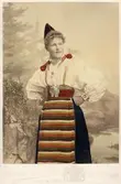 Kvinna poserar i en folkdräkt från Dalarna. Handkolorerat fotografi.