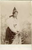 En kvinna klädd i folkdräkt från Dalarna, binder en kärve.