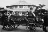 Skansen. Vårfesten 1899. Ett ekipage i öppen vagn. Några glada personer sitter i vagnen, en kusk sitter på kuskbocken. 