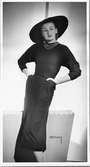 Christian Diors vårmode visas i Stockholm 1947. Kvinnlig modell i ledig pose, iklädd jumper, kjol och vidbrättad hatt. Runt halsen bär hon ett treradigt halssmycke