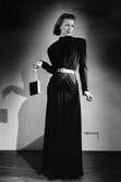 Mannekäng i svart, hellång aftonklänning med draperade detaljer och silverskärp, aftonväska i handen. NK:s Franska damskrädderi, hösten 1941.