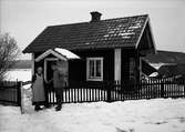 Torp med ett äldre par framför grinden, Uppland 1942