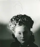 Porträtt av kvinna i hatt med flor och metallfjädrar.