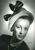 Porträtt av kvinna med hatt i rosa filt med marinblått och vitt band. Uppvisning mars 1947. Hattar använda vid franska avdelningen