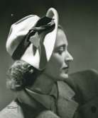 Porträtt av kvinna i hatt av Claude S:t Cyr. Beige filt med brunt band. Hatt använd vid franska avdelningens uppvisning september 1947.