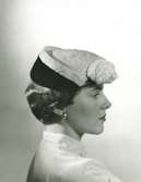 FA, Porträtt av kvinna med svart och vit hatt med dekoration framtill.