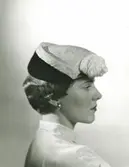 FA, Porträtt av kvinna med svart och vit hatt med dekoration framtill.