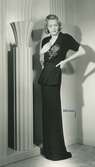 Mannekäng, Margit Langlet, i svart klänning med broderat rosmotiv och hellång kjol. Originalmodell från Francevramant, NK:s Franska damskrädderi.