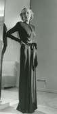 Helporträtt av kvinna i hellång aftonklänning med sidenband i midjan. Mannekängen Margit Langlet visar festplagg på NK:s Franska damskrädderi.