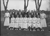 Konfirmandgrupp. Några av konfirmanderna är följande: Robert Gustafsson Frillebo, Evert Johansson Långhult, Bernt Andersson Drängsered, Olof Eliasson, Mallis Ljunggren, Eivor Schoberg, Elsebritt Schoberg och Aina Gustafsson. Kvinnan längst ut till höger heter Kirsti Silvonen och prästens efternamn är Roudén.