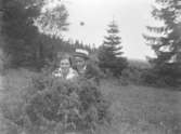 En kvinna och en man hukar bakom en enrisbuske