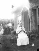 Kvinna som sitter och stickar utanför en farstukvist (ett bislag)