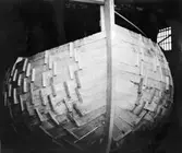 Skrivet på baksidan: Borden preliminärt hopfäst med varandra medelst påspikade klossar. När skrovskalet på så sätt blivit färdigt, lägger man in spanten och fäster dem med naglar till bordläggningen. Därefter slår man bort klossarna. Yawlbygge i Staveren, Friesland 1955.
Fotograferat av: Ruksmuseum Zuiderseemuseum Enkhuizen, Holland

Kop. finns D3:8