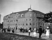 Konung Gustaf V i bilkortege från invigning av statyn på torget. På väg till regementet. Bostadshus för regementets räkning under uppförande