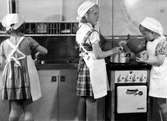 Två flickor lagar mat på en liten spis, en står vid diskbänken, kanske i en barnkrubba i Jönköping.