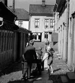 En bakgård i Jönköping. Till höger en rad torrdass och på den kullerstensbelagda gården drar några pojkar en kärra.